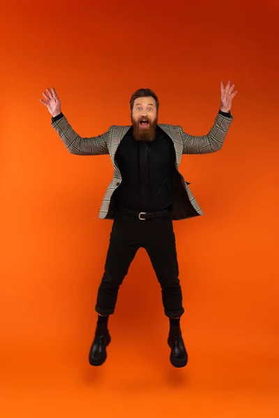 Astonished bearded man in blazer jumping on red background - foto de stock