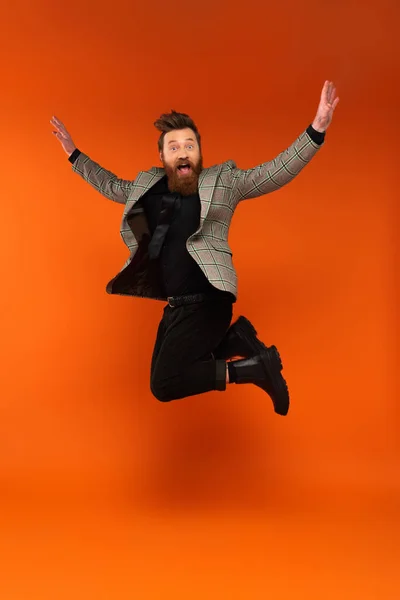 Hombre barbudo sorprendido en chaqueta a cuadros saltando sobre fondo rojo - foto de stock