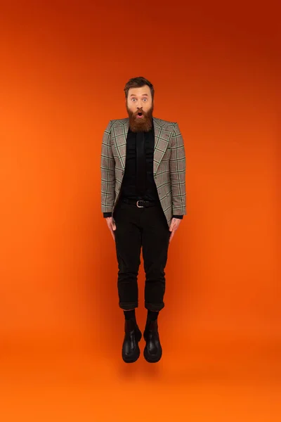 Shocked man in stylish outfit jumping on red background — Photo de stock