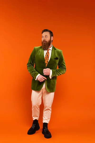 Full length of trendy bearded man adjusting jacket on red background — Stock Photo