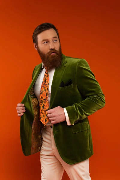 Trendy bearded man in jacket looking away isolated on red - foto de stock