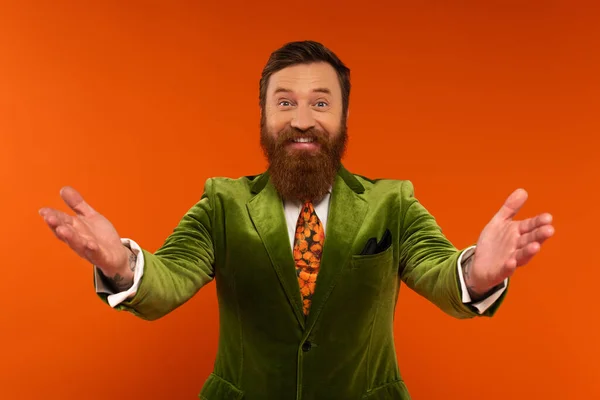Smiling bearded man in jacket outstretching hands on red background — Stock Photo