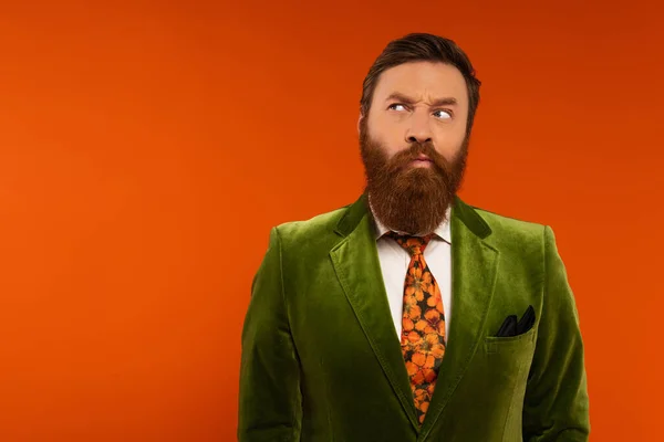 Pensive bearded model in velvet jacket looking away on red background — Stock Photo