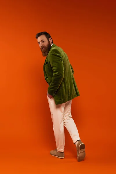Stylish bearded man in jacket walking on red background — Stock Photo