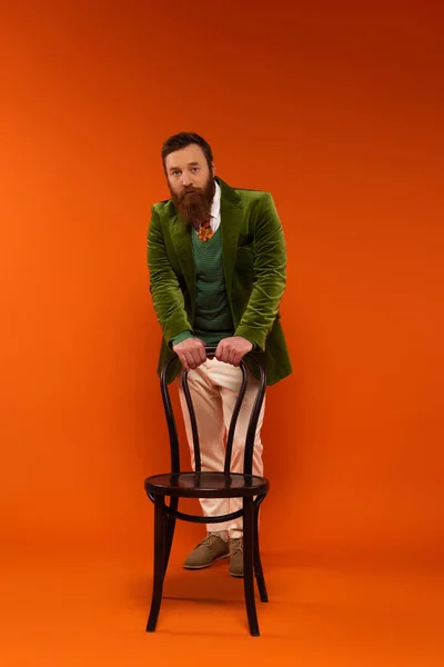 Stylish bearded model looking at camera near chair on red background — Photo de stock