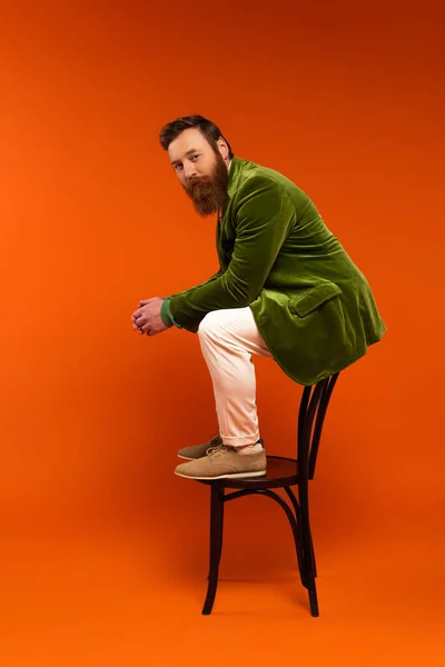 Fashionable man sitting on chair and looking at camera on red background — Stock Photo