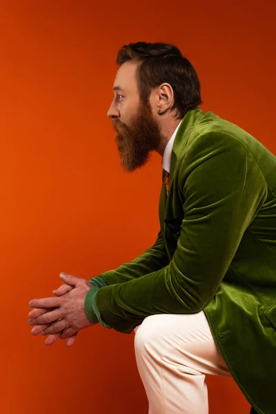 Seitenansicht eines bärtigen Mannes im stylischen grünen Blazer, der auf rotem Hintergrund wegschaut — Stockfoto
