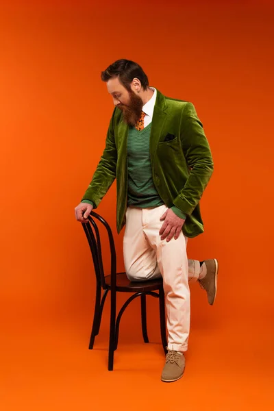 Seitenansicht des trendigen Mannes in grüner Jacke mit Blick auf Holzstuhl auf rotem Hintergrund — Stockfoto