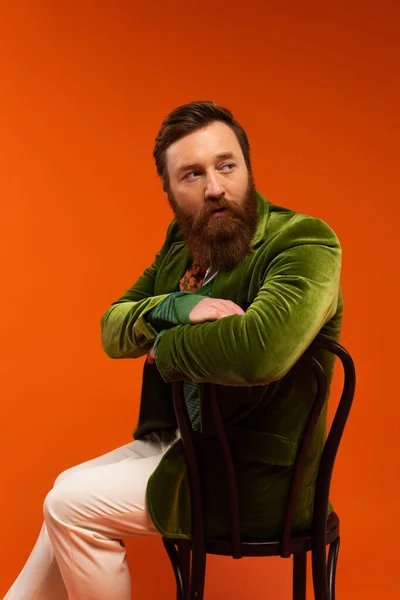 Portrait of stylish bearded man sitting on chair on red background — Stock Photo