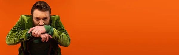 Дорослий чоловік у зеленій оксамитовій куртці, що сидить на стільці на червоному тлі, банер — стокове фото