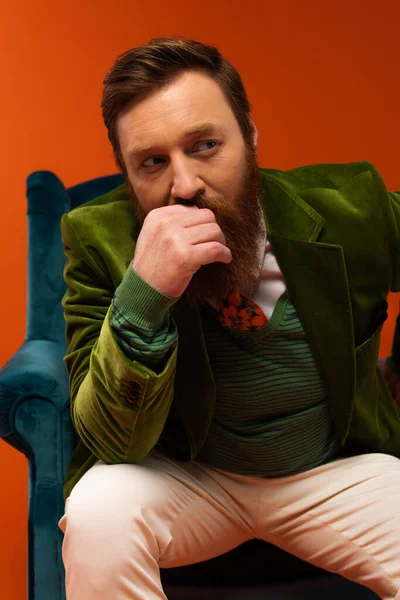 Fashionable bearded man sitting on blurred armchair on red background - foto de stock