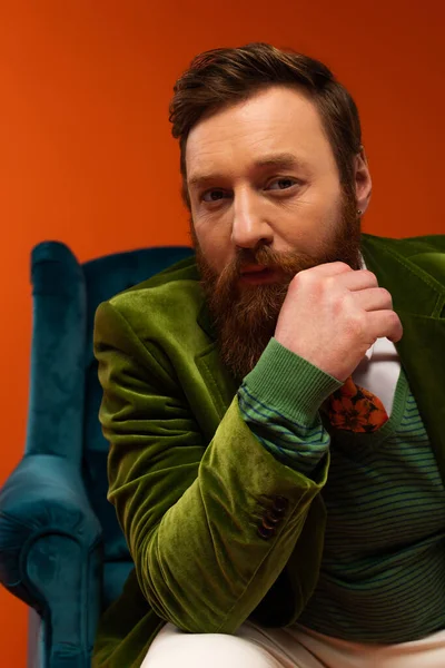 Portrait of stylish bearded model looking at camera near blurred armchair on red background - foto de stock