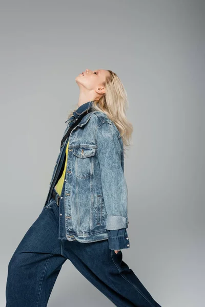 Young blonde woman in stylish denim jacket posing with raised head isolated on grey — Fotografia de Stock