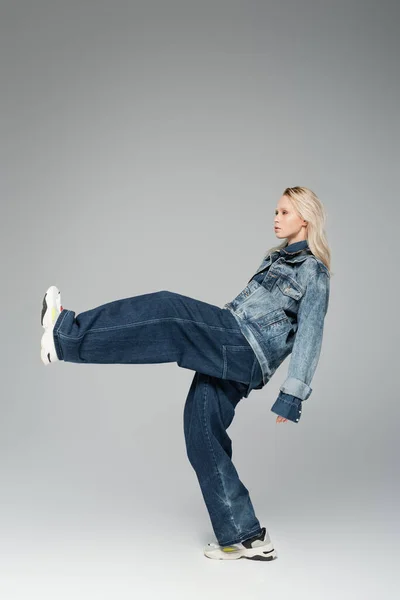 Junges blondes Model in stylischem Jeans-Outfit und Turnschuhen posiert auf grau — Stockfoto