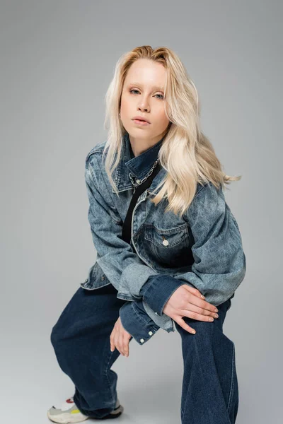 Young blonde model in trendy denim outfit looking at camera isolated on grey — Stock Photo