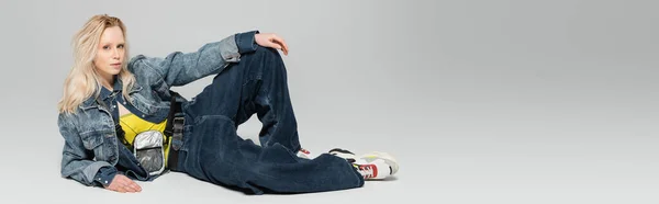 Full length of young blonde woman in blue denim outfit and trendy sneakers posing on grey background, banner — Photo de stock