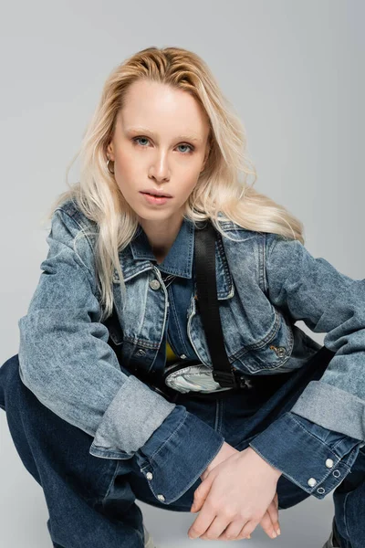 Blonde albino woman in stylish denim jacket with belt bag posing isolated on grey — Stock Photo