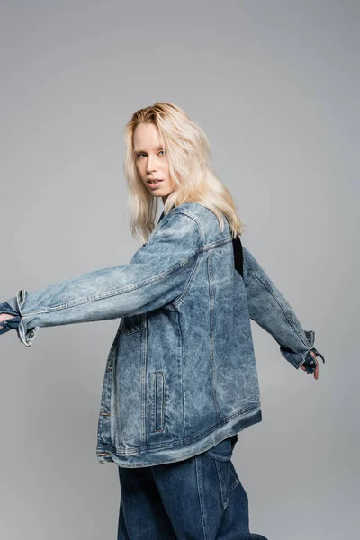 Young blonde woman in denim blue jacket posing with outstretched hands isolated on grey — Stockfoto