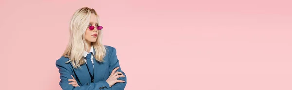 Blonde woman in blue blazer with tie and sunglasses posing with crossed arms isolated on pink, banner — Stock Photo