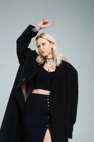 Jovem mulher loira na moda casaco preto olhando para longe e gesto isolado no cinza — Fotografia de Stock