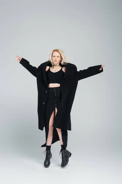Full length of blonde and young woman in stylish black outfit levitating on grey — Stock Photo