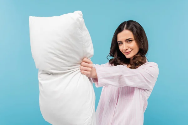 Brunette young woman in pajamas holding white pillow isolated on blue — Foto stock