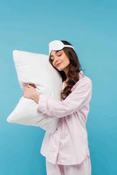 Mujer joven en pijama y máscara de noche durmiendo en almohada blanca aislada en azul - foto de stock