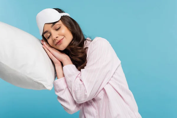 Jovem mulher satisfeita em pijama e máscara noite dormindo no travesseiro branco isolado em azul — Fotografia de Stock