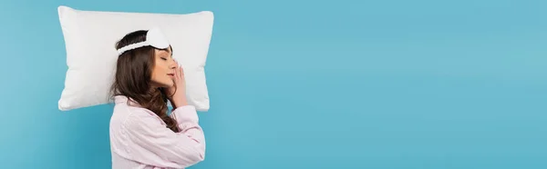 Side view of brunette woman in pajamas and night mask sleeping on white pillow isolated on blue, banner — Photo de stock
