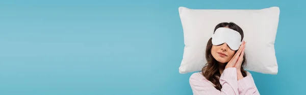 Young woman in pajamas and night mask resting on white pillow isolated on blue, banner - foto de stock