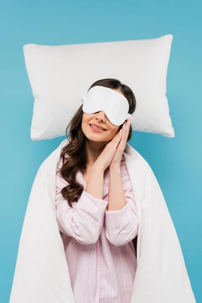Mujer joven cubierta de edredón blanco durmiendo en máscara de noche en almohada blanca aislada en azul - foto de stock