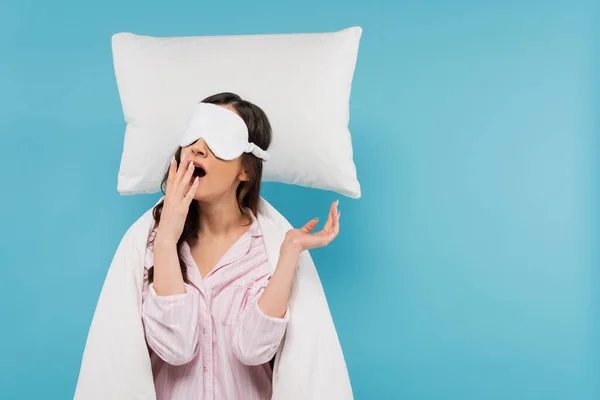 Young woman in night mask yawning near levitating pillow isolated on blue — Stock Photo
