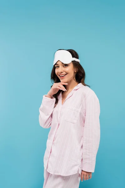 Happy young woman in night mask and pajamas isolated on blue — Stock Photo