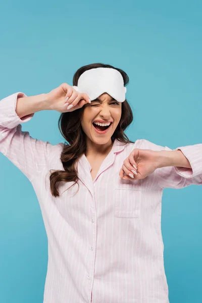 Excited young woman in pajamas adjusting night mask isolated on blue — Stock Photo