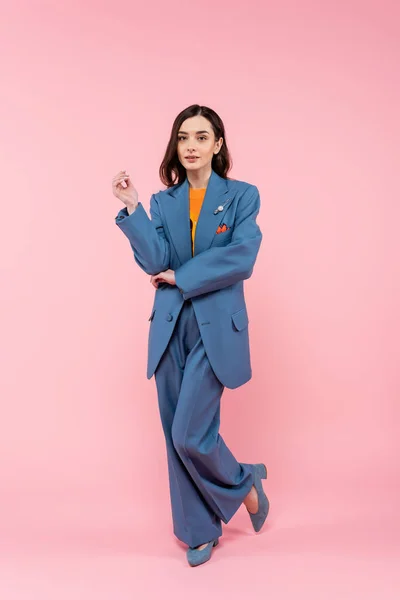 Full length of young brunette woman in blue pantsuit standing on pink - foto de stock