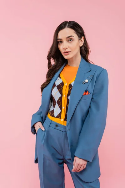 Young brunette woman in blue pantsuit standing with hand in pocket isolated on pink — Fotografia de Stock