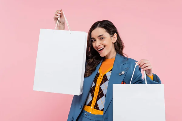 Pleased young woman in blue blazer holding shopping bags isolated on pink — Stock Photo