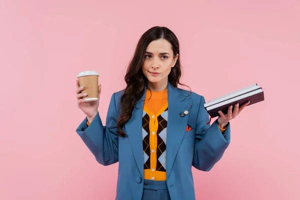 Displeased manager in blue blazer holding notebooks and paper cup isolated on pink — Stock Photo