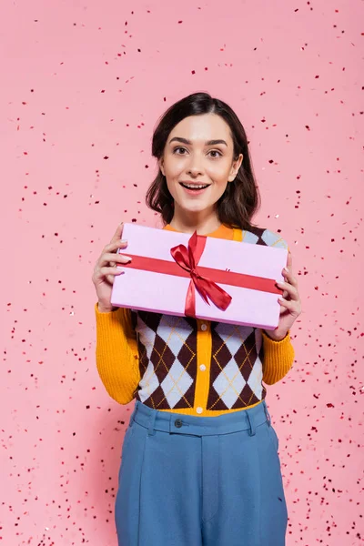 Happy and stylish woman holding gift box with red ribbon on pink background — Stock Photo