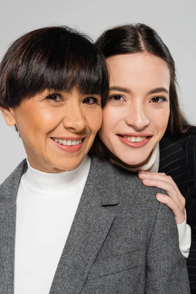 Portrait of happy asian mother and daughter in blazers smiling at camera isolated on grey — Stock Photo