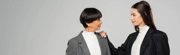 Positive asian woman in stylish clothes touching shoulder of brunette mother isolated on grey, banner — Stock Photo
