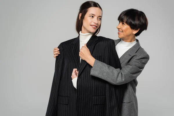 Smiling asian woman covering young daughter with black blazer isolated on grey — Stock Photo