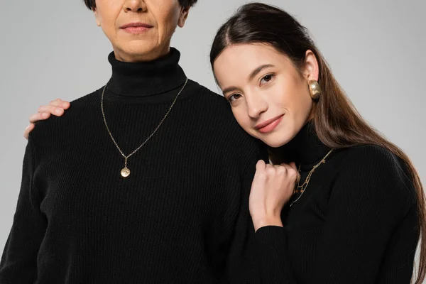 Happy asian woman in black turtleneck and necklaces hugging mother and looking at camera isolated on grey — Stock Photo