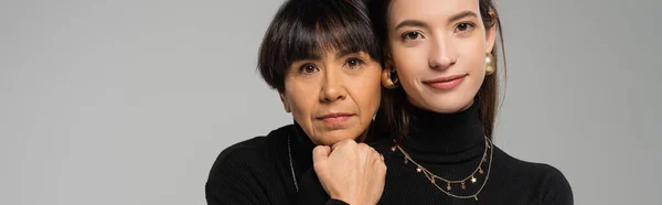 Portrait of young brunette woman with trendy asian mother looking at camera isolated on grey, banner — Fotografia de Stock