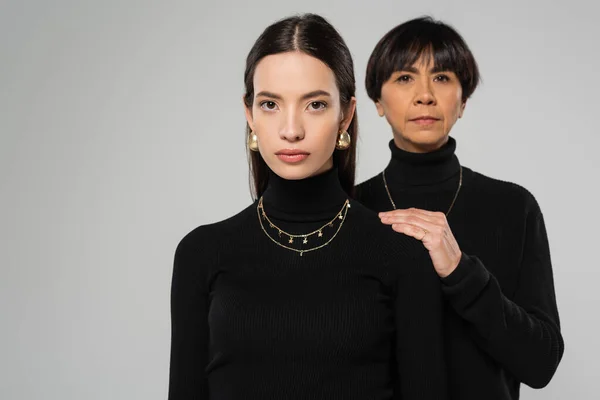 Middle aged asian woman touching shoulder of young brunette daughter isolated on grey — Stock Photo