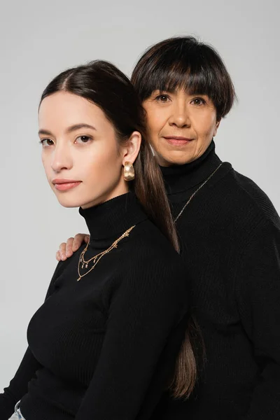 Portrait of stylish asian mother and daughter wearing black turtlenecks and necklaces isolated on grey — Fotografia de Stock