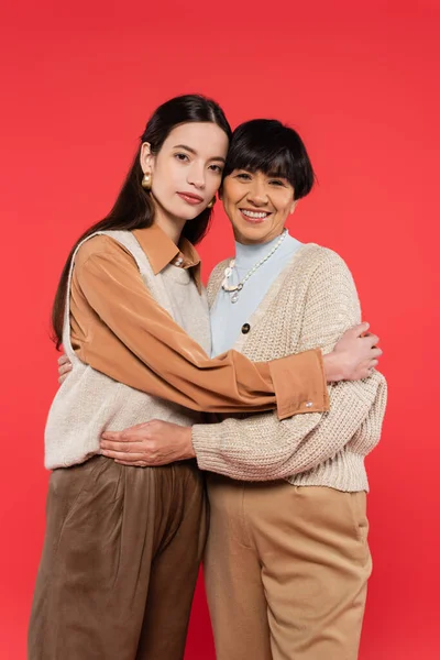 Asian mother and daughter in stylish casual outfit embracing and looking at camera isolated on coral — Foto stock