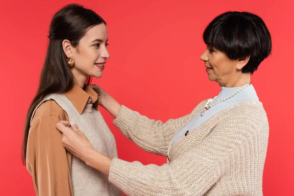 Middle aged asian woman adjusting vest on smiling brunette woman isolated on coral — Photo de stock