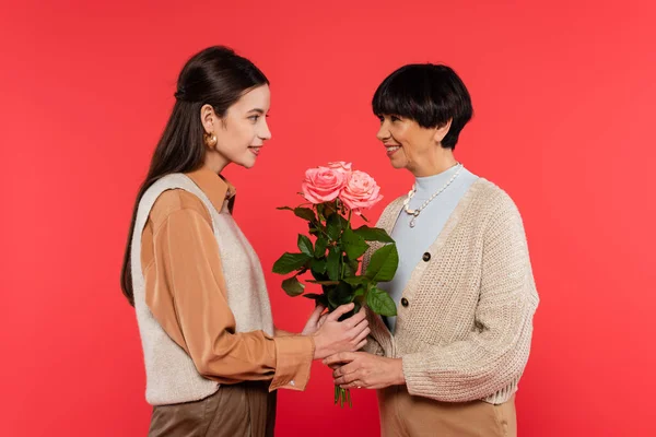 Happy asian and young woman giving bouquet of flowers to cheerful mother isolated on coral — Stock Photo