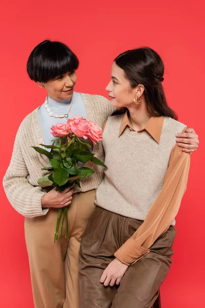 Cheerful asian mother with bouquet of flowers hugging happy daughter isolated on coral — Foto stock